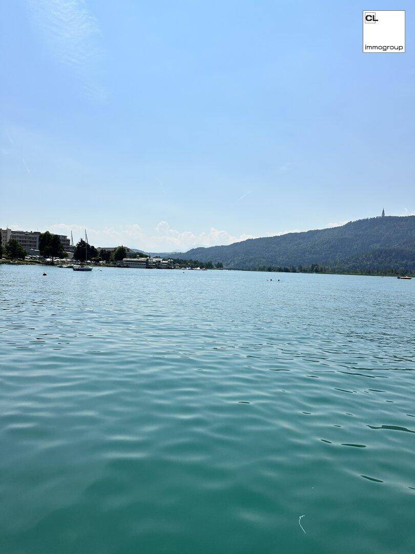 Weitläufiger Blick über den See mit bewaldeten Bergen und vereinzelten Gebäuden am Ufer.