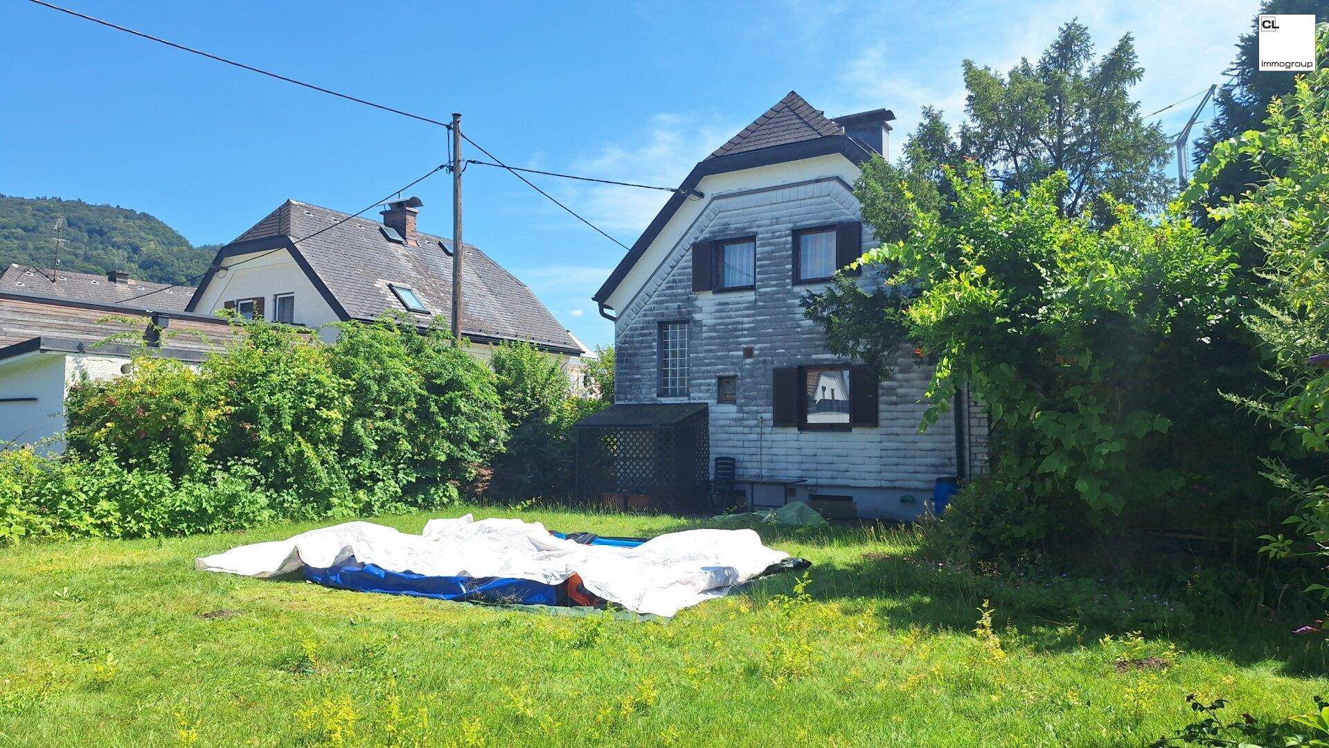 Rückansicht des Hauses mit großem Rasenbereich und üppiger Vegetation im Garten.