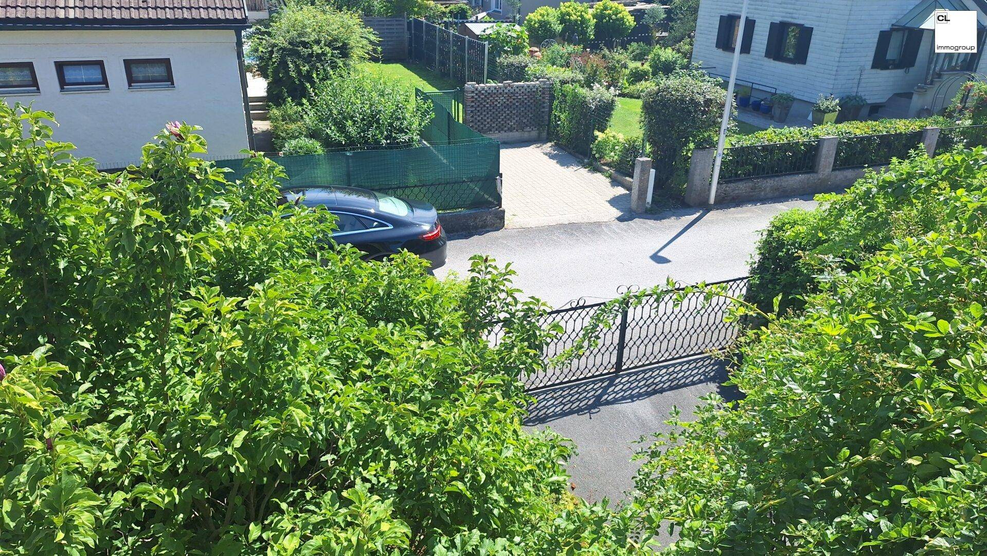Zufahrt zum Grundstück mit einem schmiedeeisernen Tor, gepflegter Hecke und parkendem Auto.