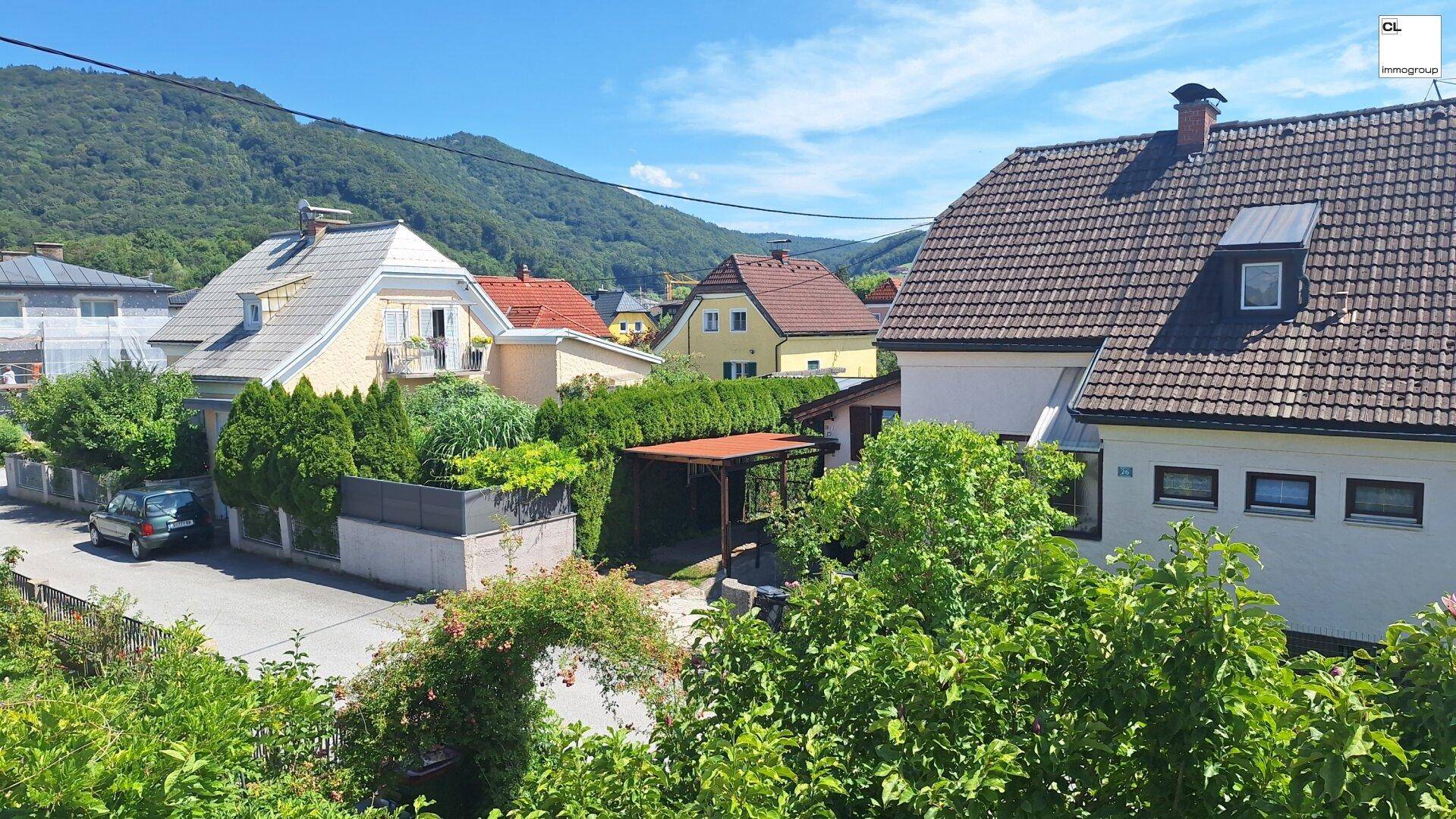 Panoramablick über die Wohnsiedlung mit grünen Hügeln und Bergen im Hintergrund unter blauem Himmel.