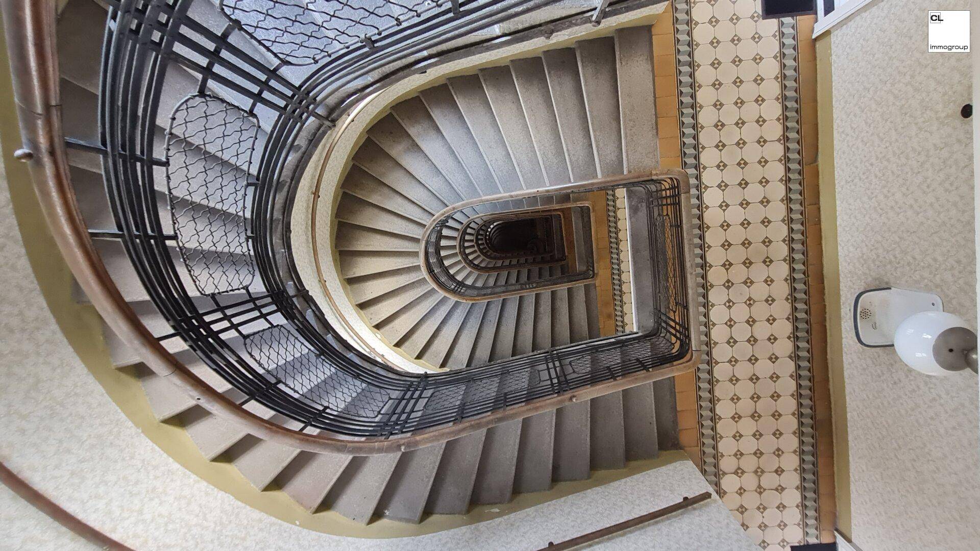 Blick von oben auf ein kunstvolles Wendeltreppenhaus mit detailliertem Geländer und Fliesenboden.