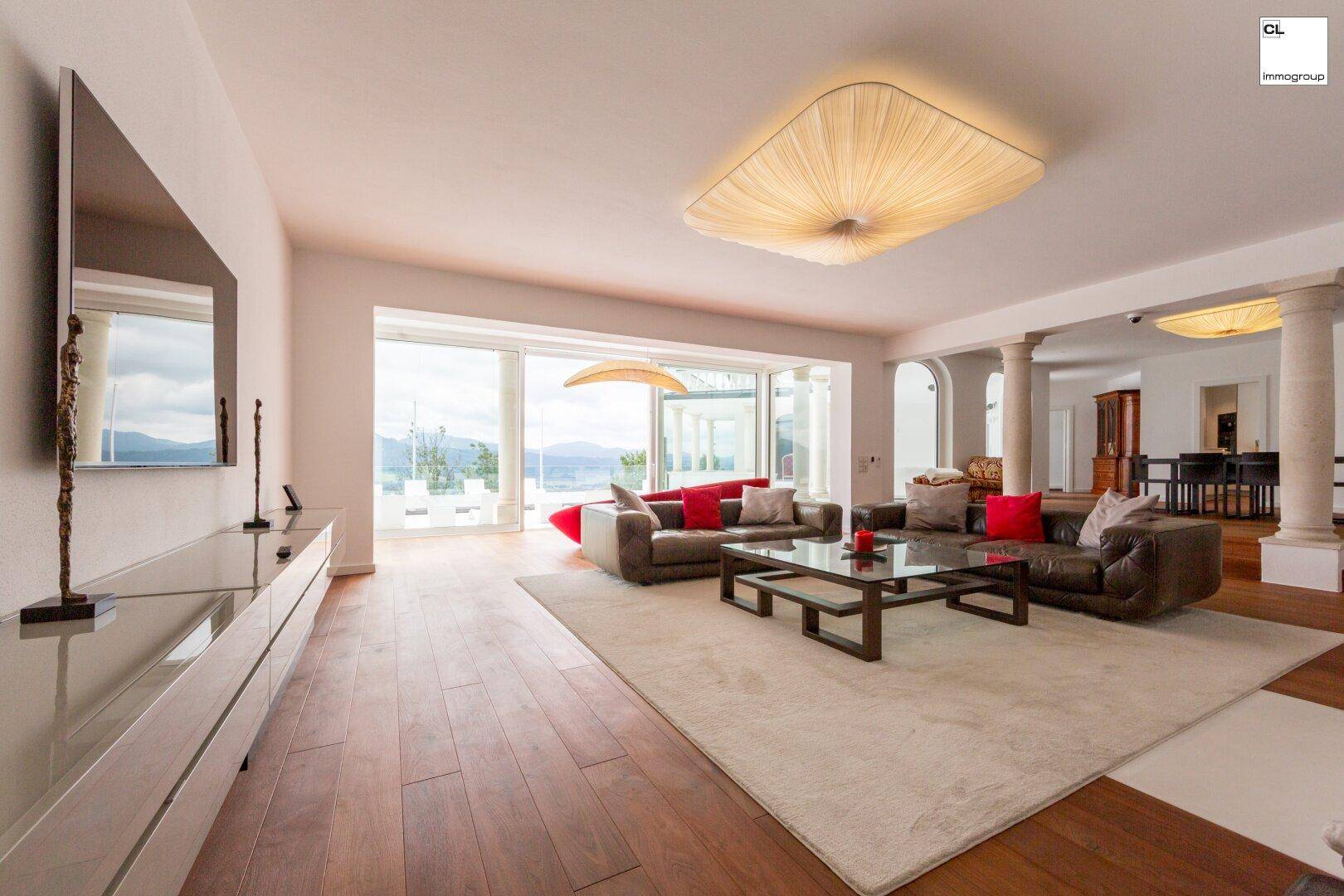 Geräumiges, helles Wohnzimmer mit Holzboden, modernen Möbeln und Zugang zu einer Terrasse mit Seeblick.