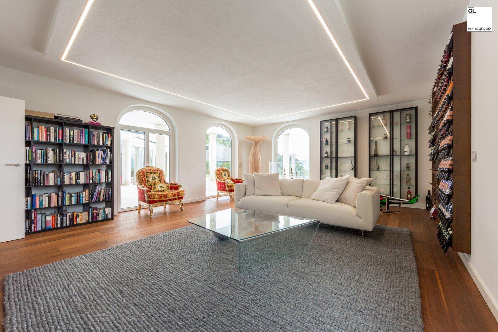 Elegantes Wohnzimmer mit Holzboden, Bücherregalen und einem großen Weinregal, hell durch Rundbogenfenster.