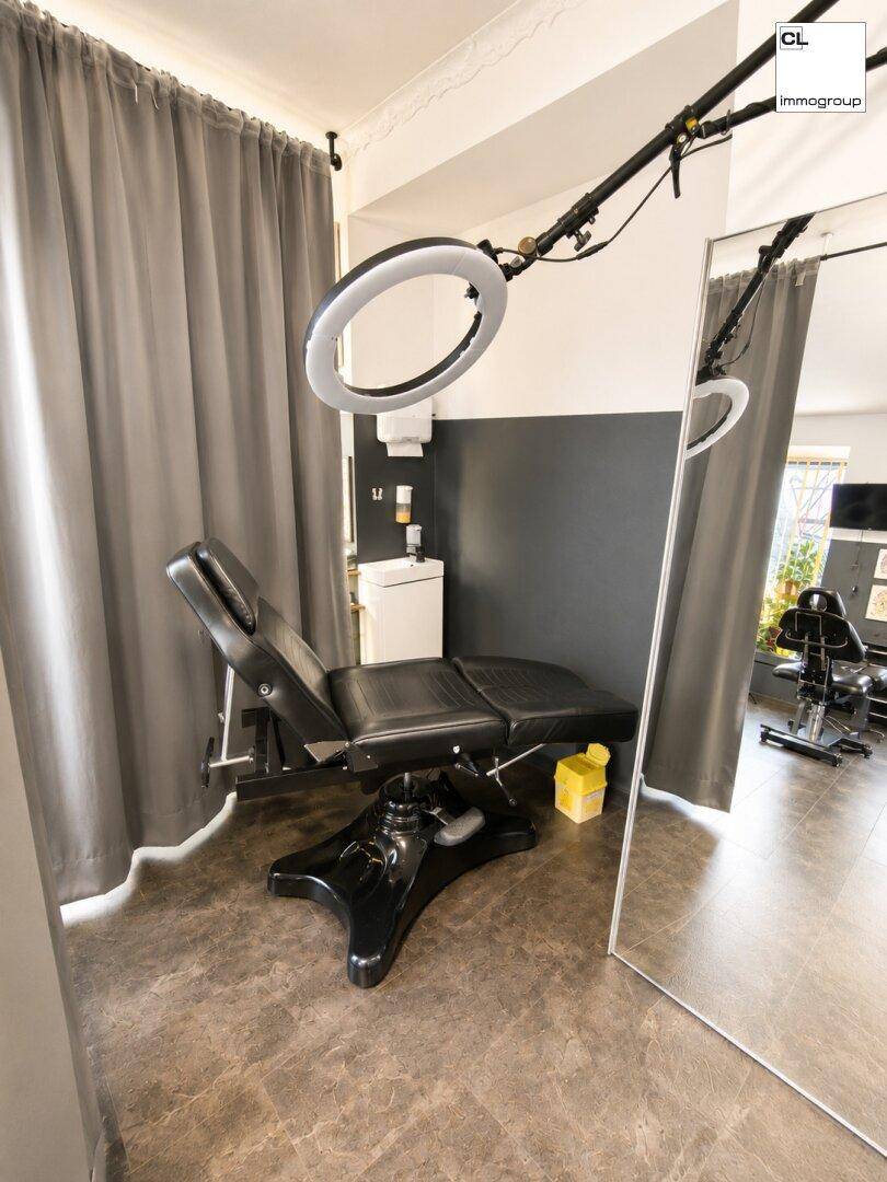 Detailansicht eines Arbeitsplatzes in einem Tattoo-Studio mit Liege, großem Spiegel und Vorhängen für Privatsphäre.
