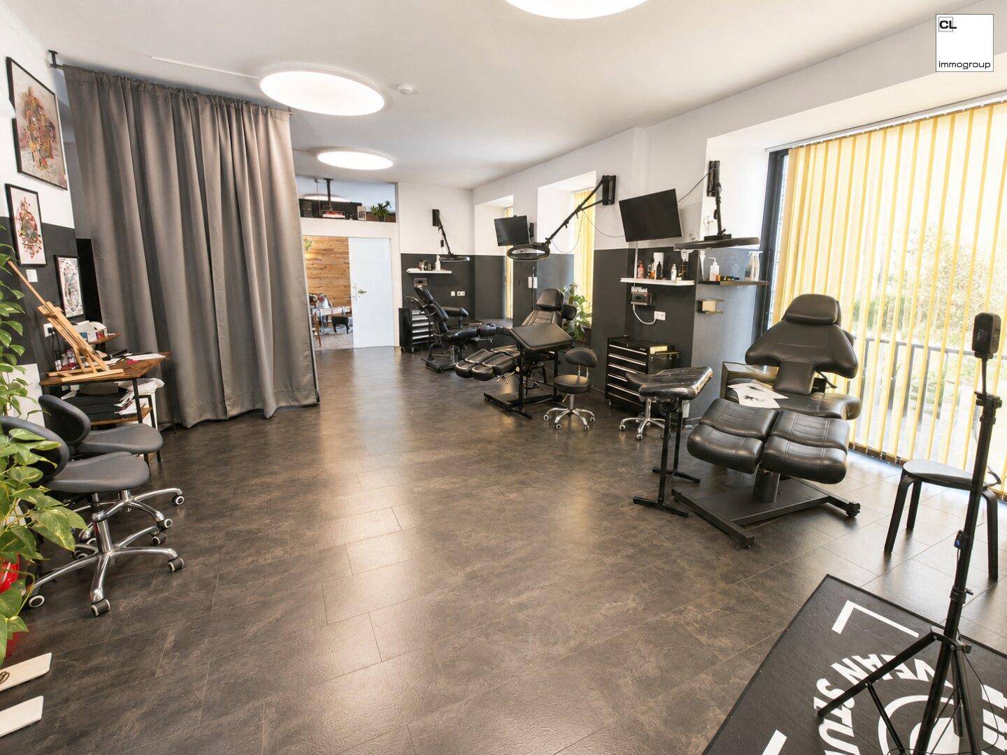 Geräumiger Arbeitsbereich in einem Tattoo-Studio mit mehreren Stationen und großen Fenstern, die viel Licht hereinlassen.