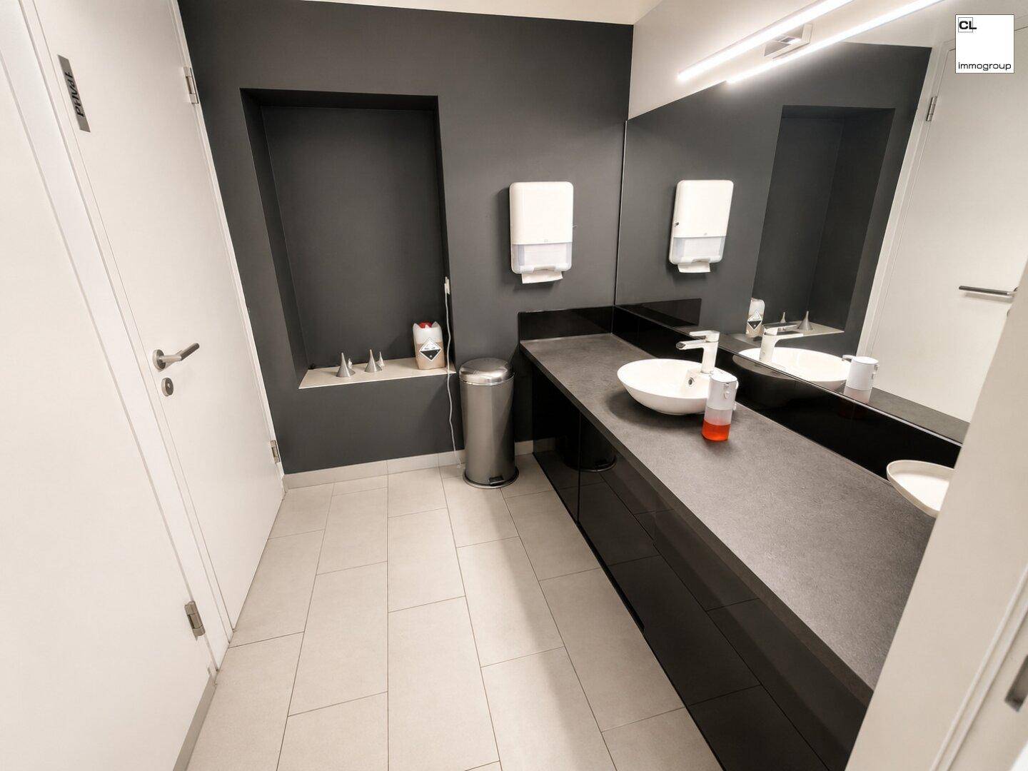 Modernes Badezimmer mit dunklem Waschtisch, großem Spiegel und weißen Fliesen, sehr sauber und funktional.