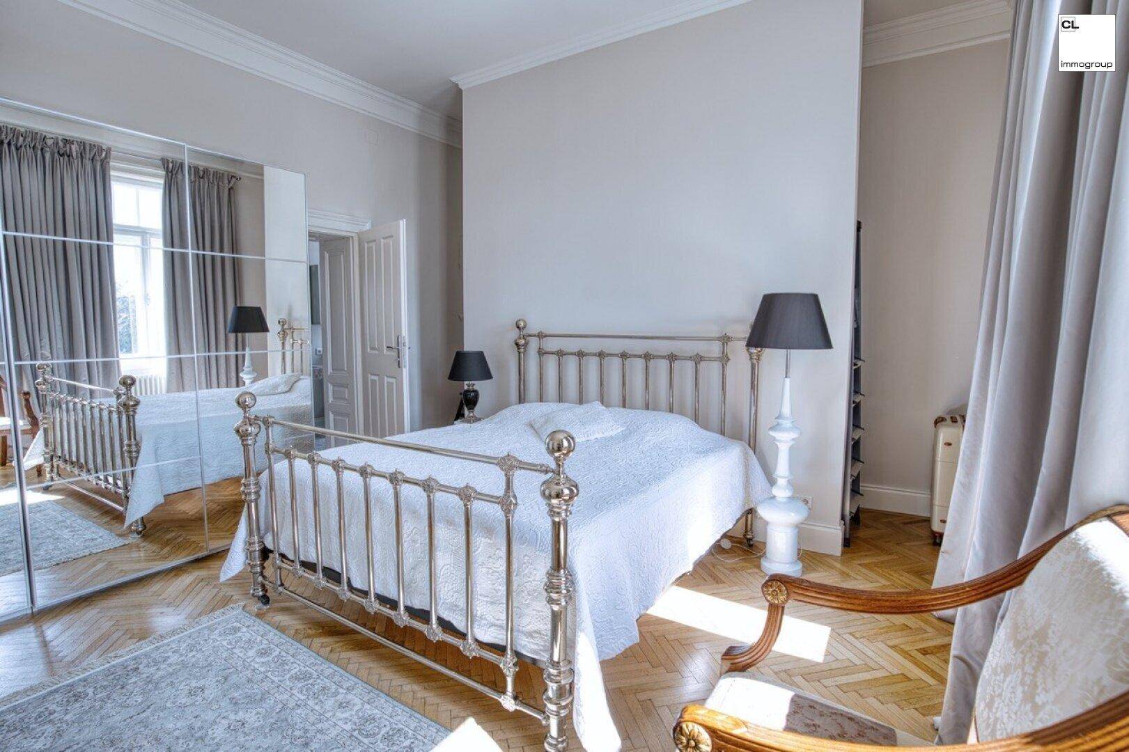 Elegantes Schlafzimmer mit klassischem Metallbett, Spiegelschrank und Fischgrätparkett.