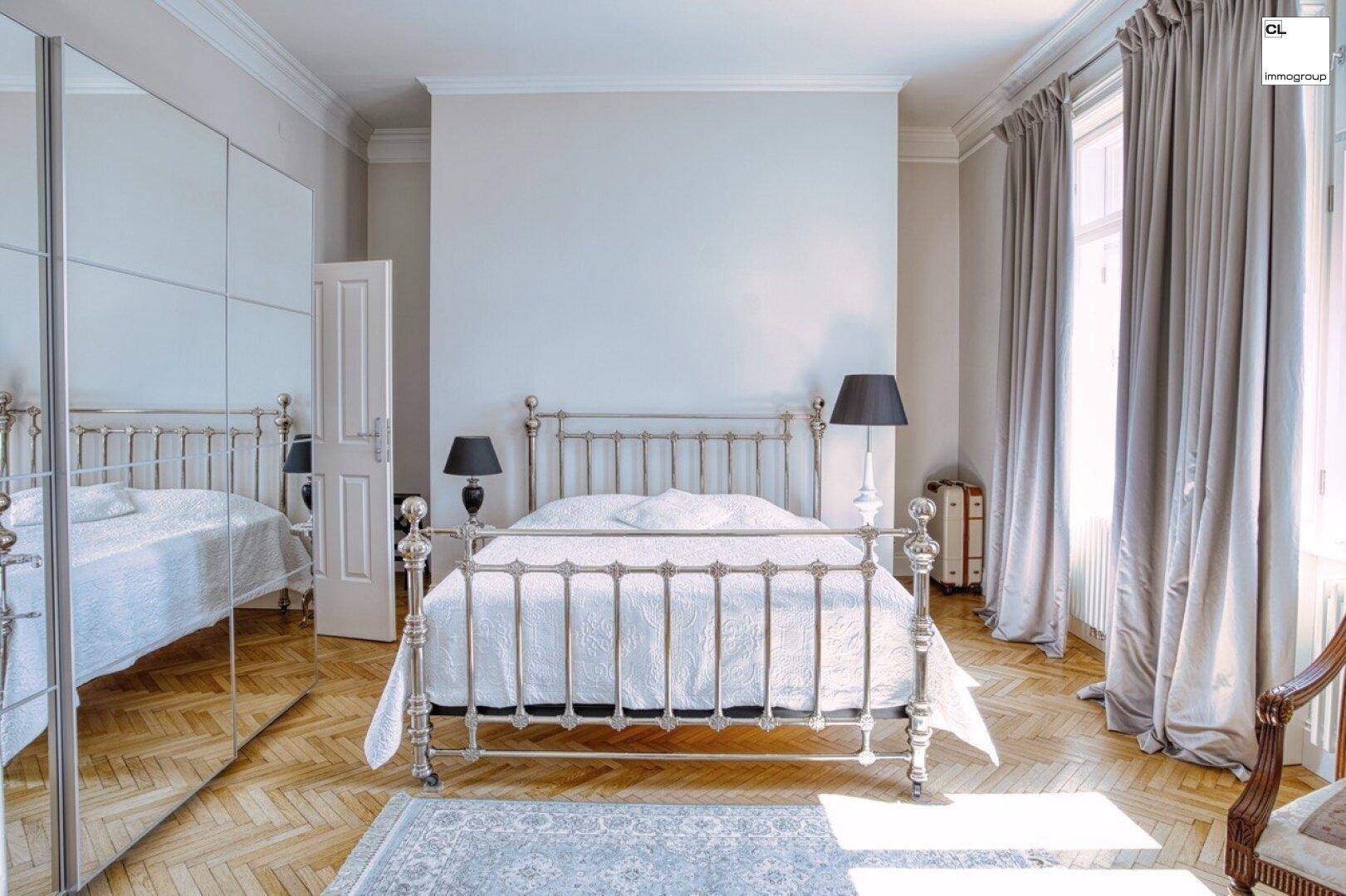 Helles Schlafzimmer mit Fischgrätparkett, hohen Decken und einem großen Spiegelschrank.