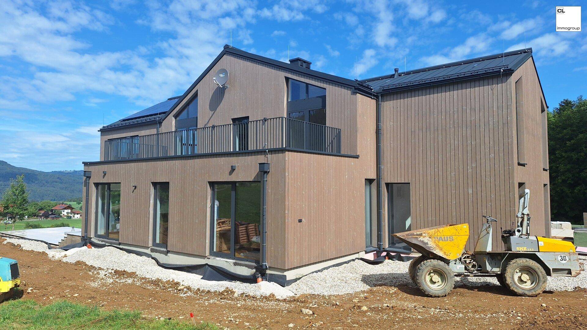 Seitenansicht des im Bau befindlichen Hauses mit Holzverkleidung und großen Glasflächen.