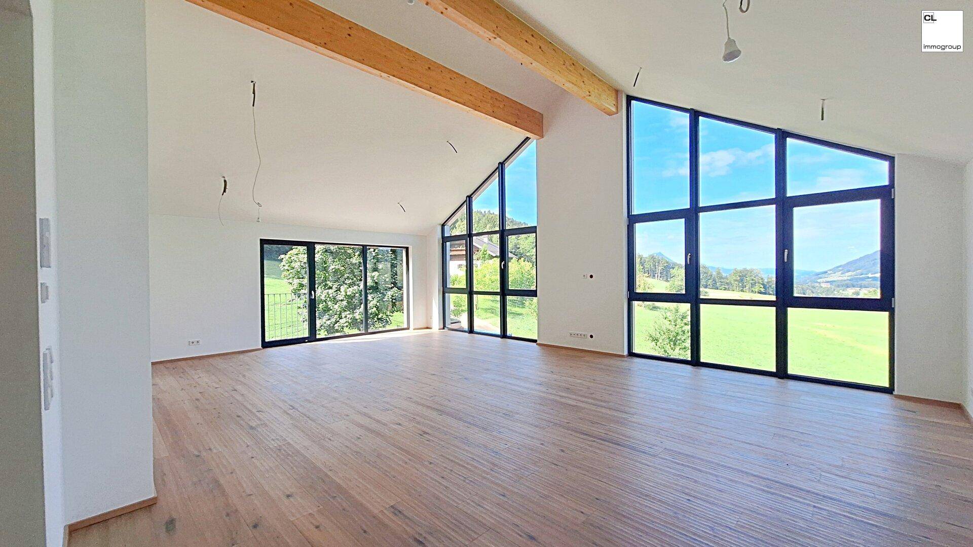 Geräumiges Wohnzimmer mit hohen Decken, Holzbalken und großen Fenstern mit Landschaftsblick.