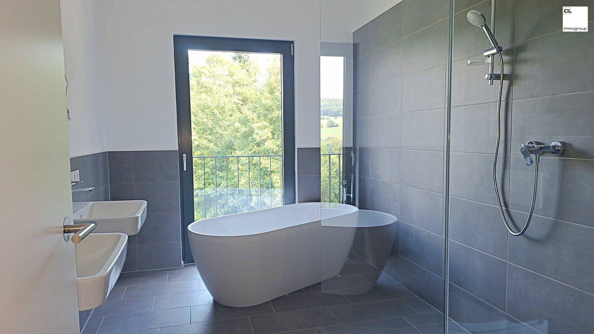 Modernes Badezimmer mit freistehender Badewanne, Dusche und Fenster mit Waldblick.