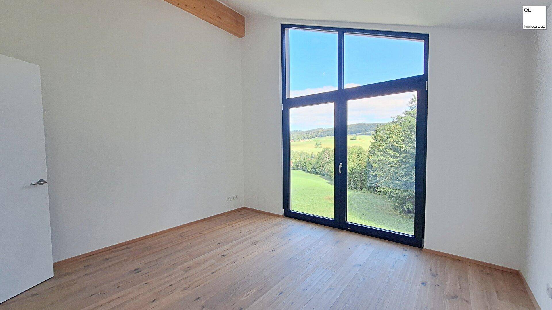 Geräumiges Schlafzimmer mit Holzboden und weitem Blick über die grüne Landschaft.