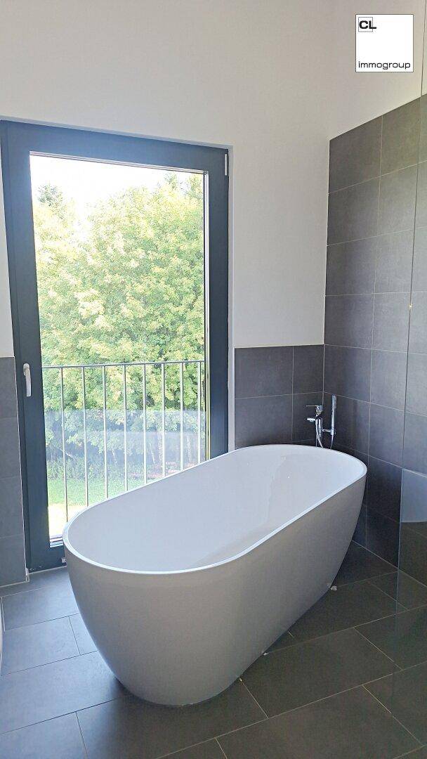 Modernes Badezimmer mit freistehender Badewanne und Fenster mit Blick ins Grüne.