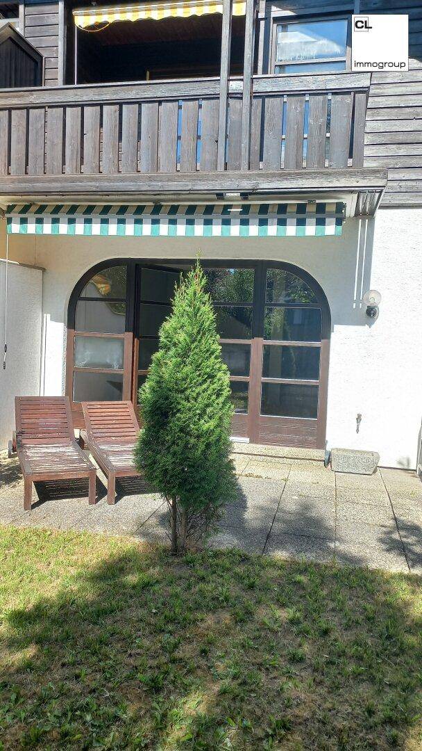 Sonniger Terrassenbereich mit Liegestühlen und Zugang zum Garten, umgeben von üppigem Grün.