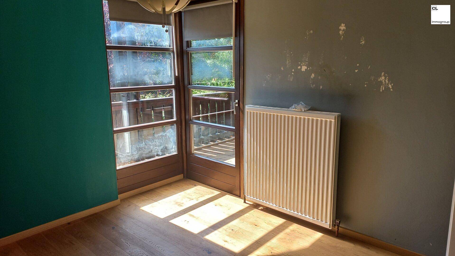 Zimmer mit Holzboden und Balkonzugang, benötigt Renovierung der Wände, aber hell und geräumig.