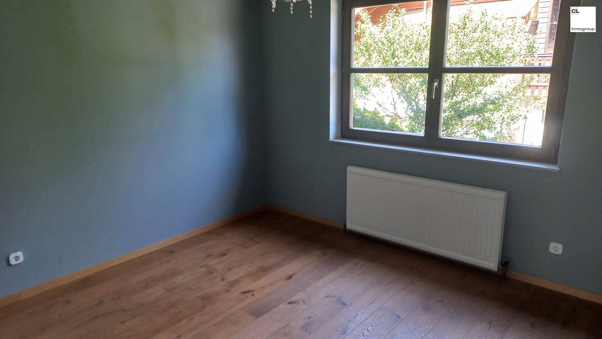 Helles Schlafzimmer mit Holzboden und großem Fenster, bietet einen ruhigen Ausblick ins Grüne.