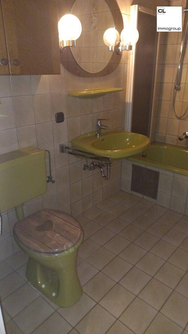 Badezimmer im 80er-Jahre-Stil mit grüner Keramik und Fliesenboden, inklusive Badewanne und WC.