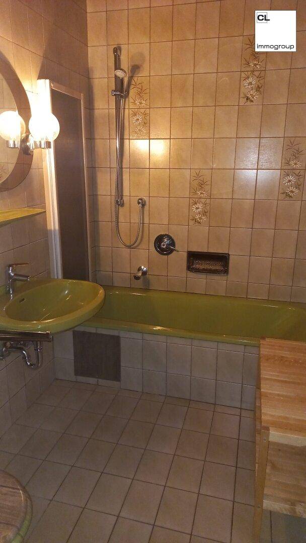 Badezimmer mit Badewanne und Duschfunktion, Fliesenboden und grünen Sanitärobjekten im Retro-Stil.