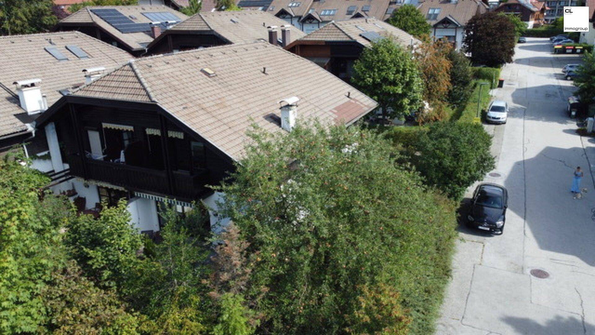Luftaufnahme eines Hauses mit Satteldach und dunkler Holzfassade, umgeben von viel Grün.