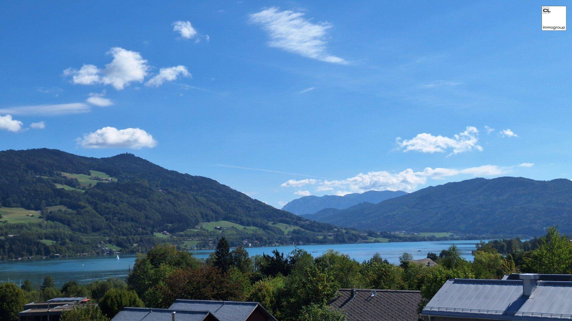 Weiter Blick über den See und die umliegende Berglandschaft an einem sonnigen Tag mit wenigen Wolken.