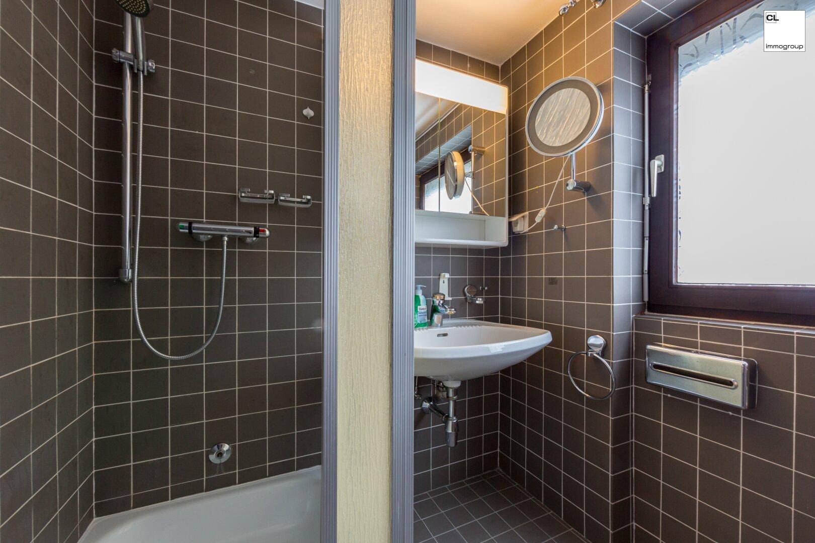 Kleines Badezimmer mit Dusche, braunen Fliesen und Fenster für natürliches Tageslicht.