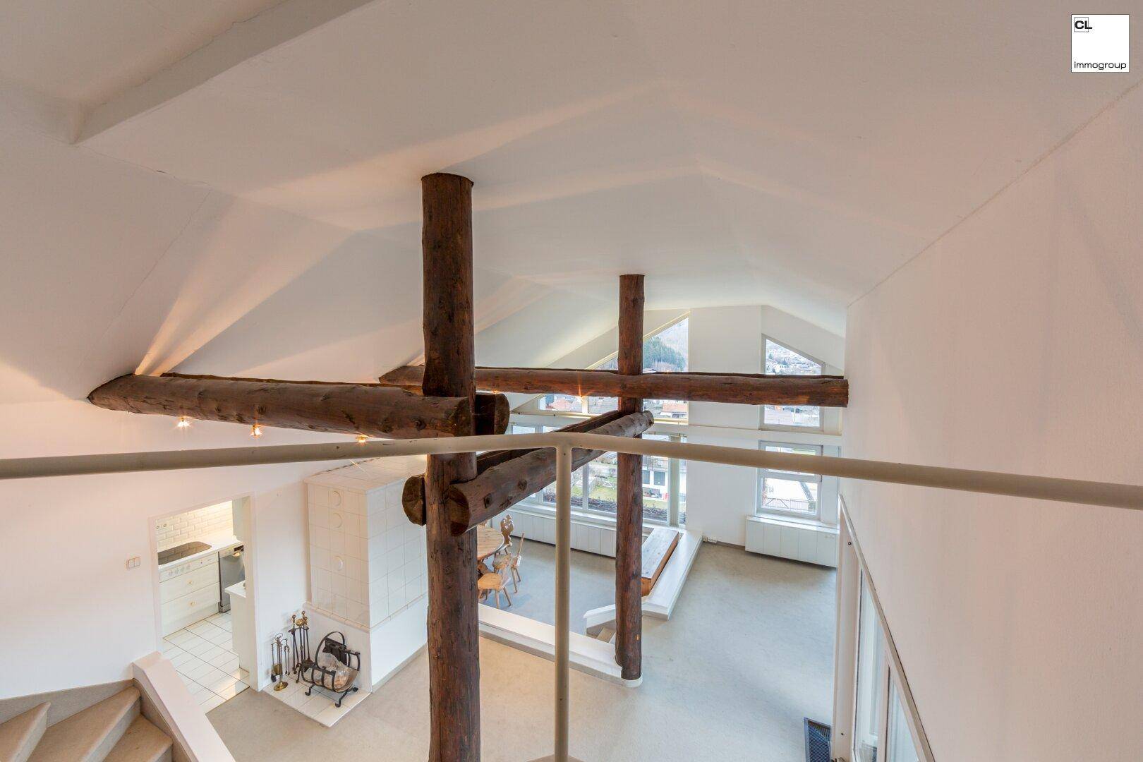 Blick von der Galerie in den offenen Wohnbereich mit markanten Holzbalken und großen Fenstern.
