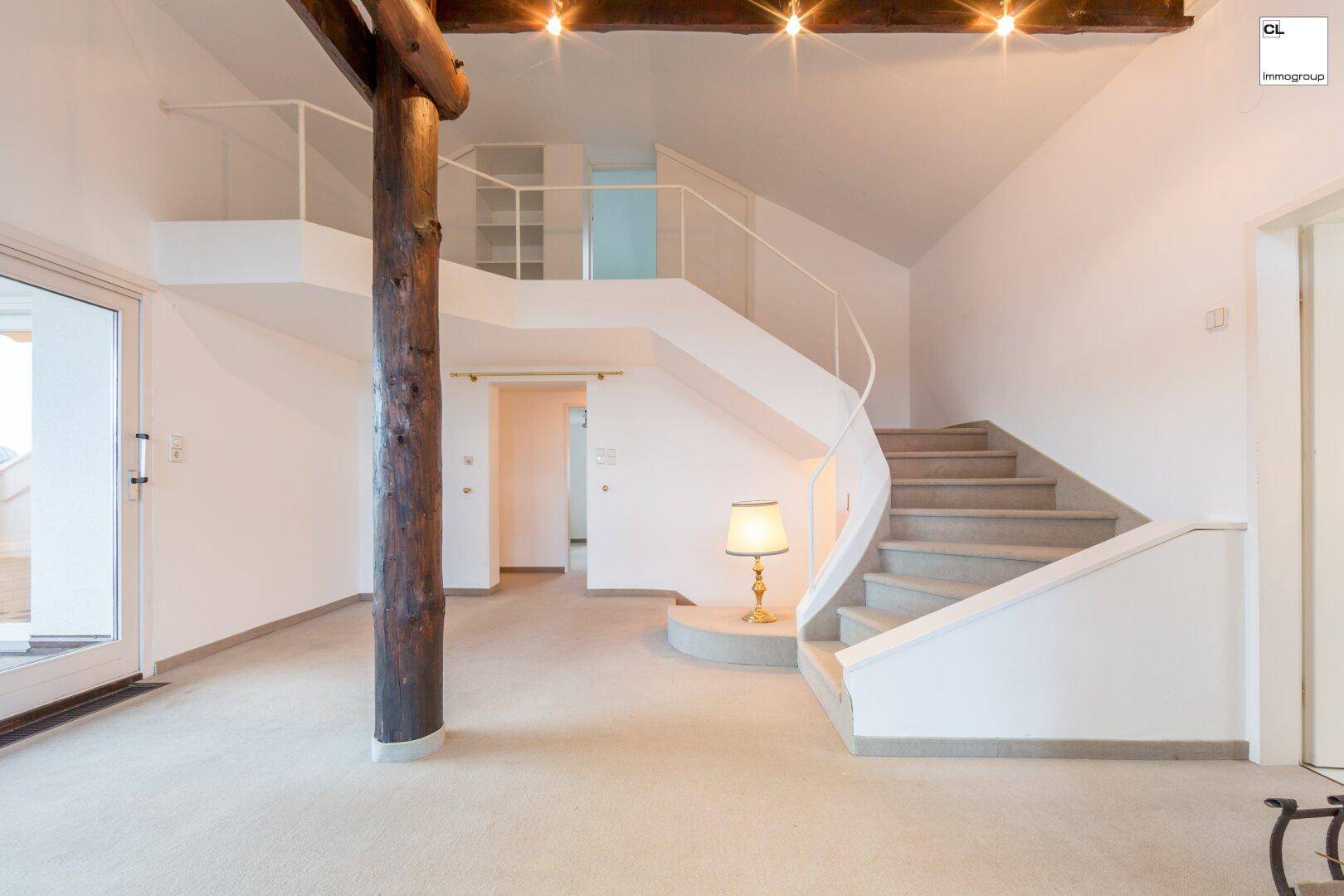 Heller Eingangsbereich mit eleganter Wendeltreppe und markantem Holzbalken als architektonisches Element.