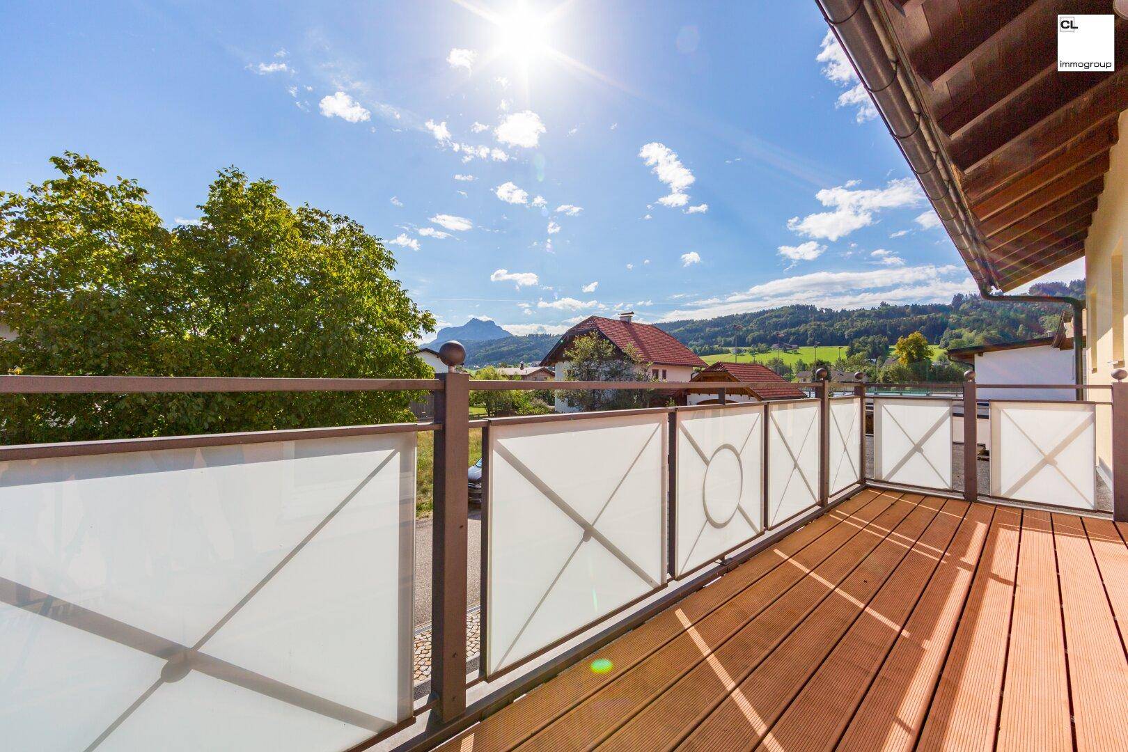 Sonniger Balkon mit Holzboden und weitem Blick auf die umliegende Berglandschaft.