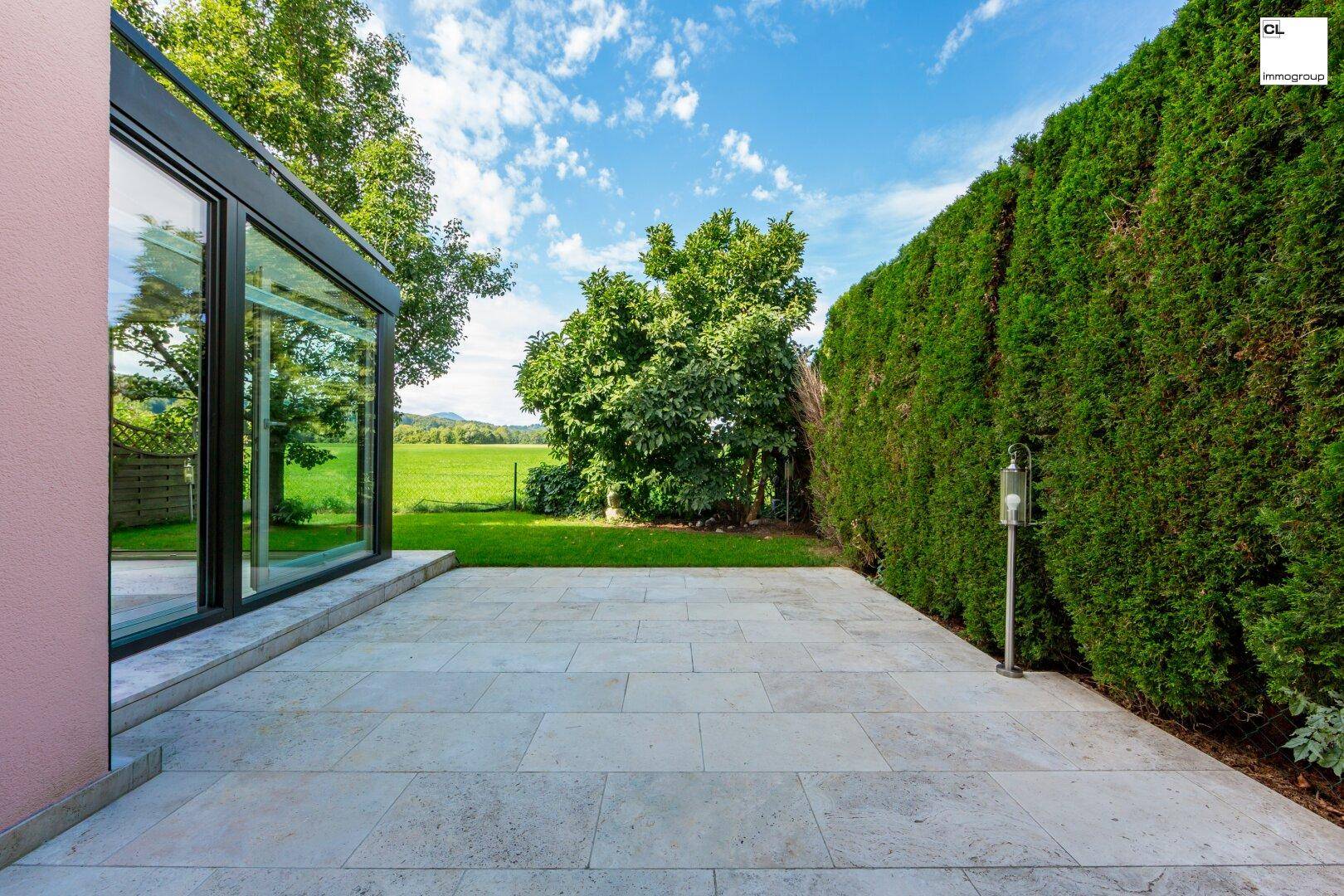 Große gepflasterte Terrasse neben dem Wintergarten mit Blick ins Grüne und Hecke.