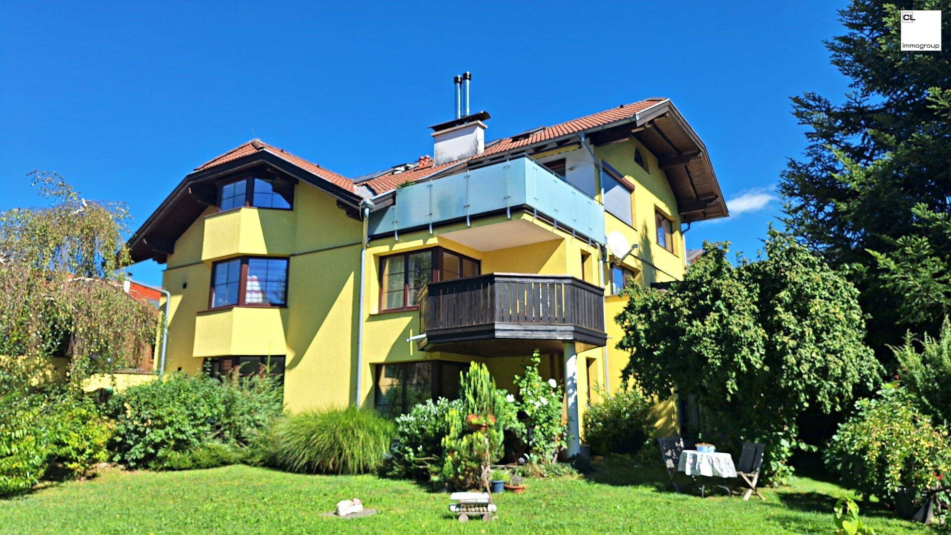 Gelbes Wohnhaus mit Balkonen und gepflegtem Gartenbereich unter strahlend blauem Himmel.