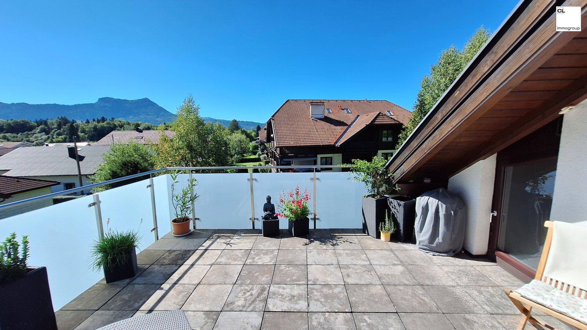 Geräumige Terrasse mit Fliesenboden, Pflanzen und Blick auf die umliegende Wohnbebauung und Berge.