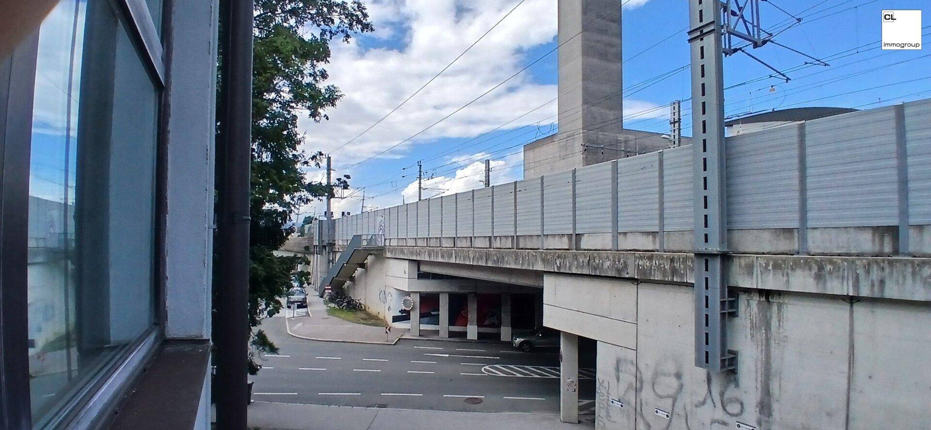 Ausblick auf eine Eisenbahnbrücke mit darunterliegender Straße und einer Lärmschutzwand.
