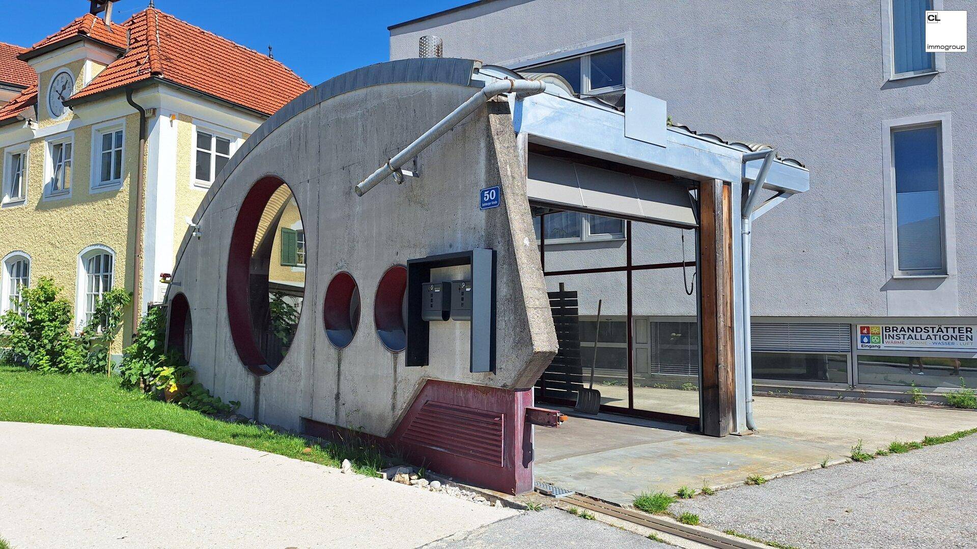 Einzigartige Fassade mit geschwungener Betonstruktur und großer Glasfront, daneben ein traditionelles Gebäude.