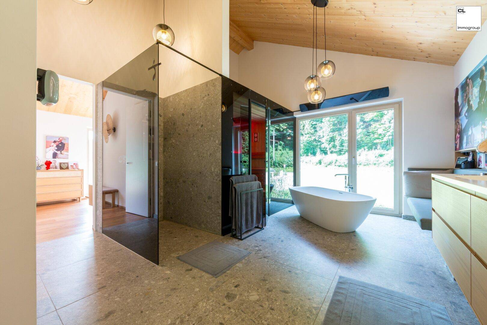 Luxuriöses Badezimmer mit freistehender Badewanne, Glasdusche und Sauna sowie Blick ins Grüne.