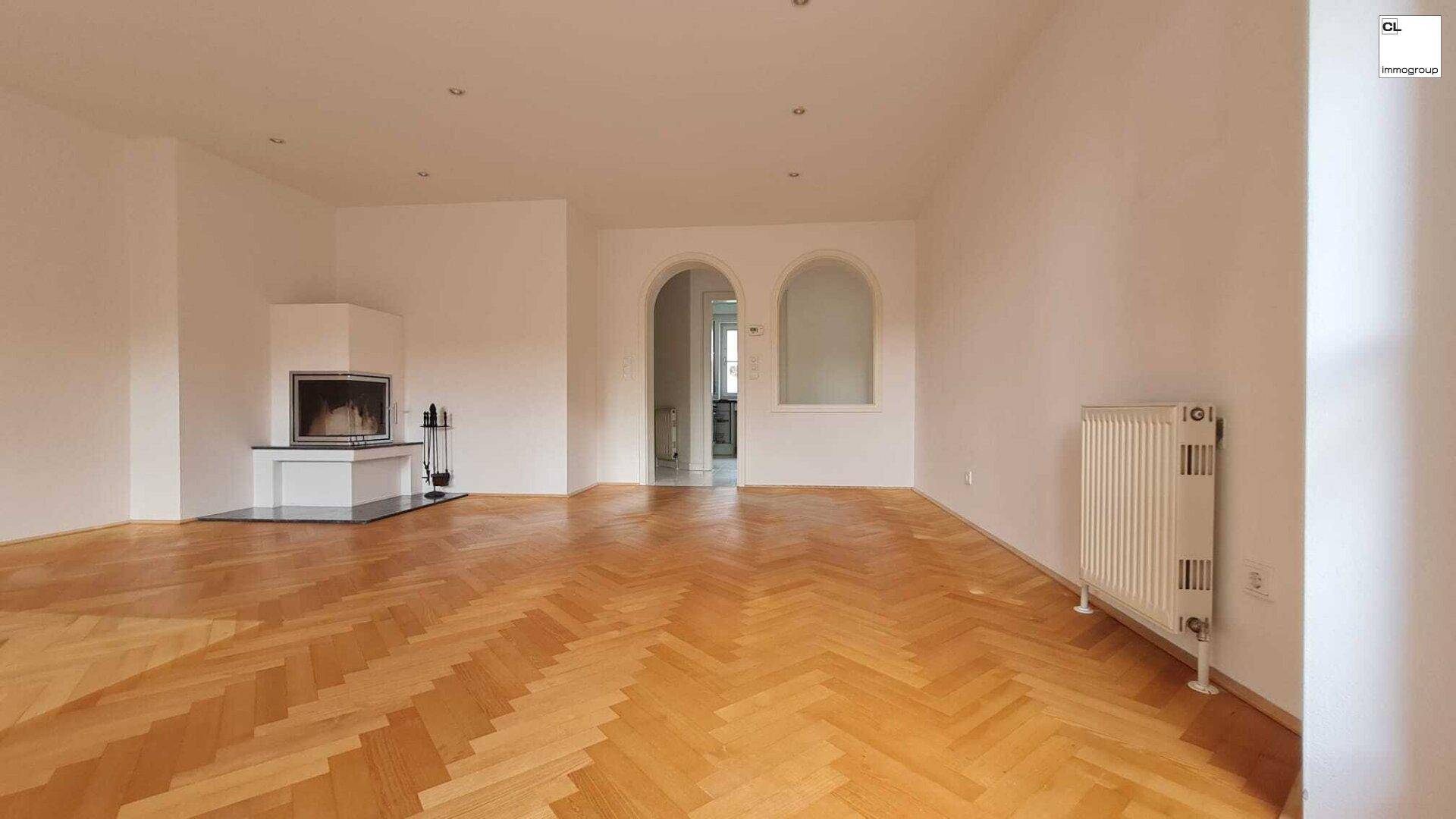 Geräumiges Wohnzimmer mit Kamin, Fischgrätparkett und Durchgängen zu weiteren Räumen.