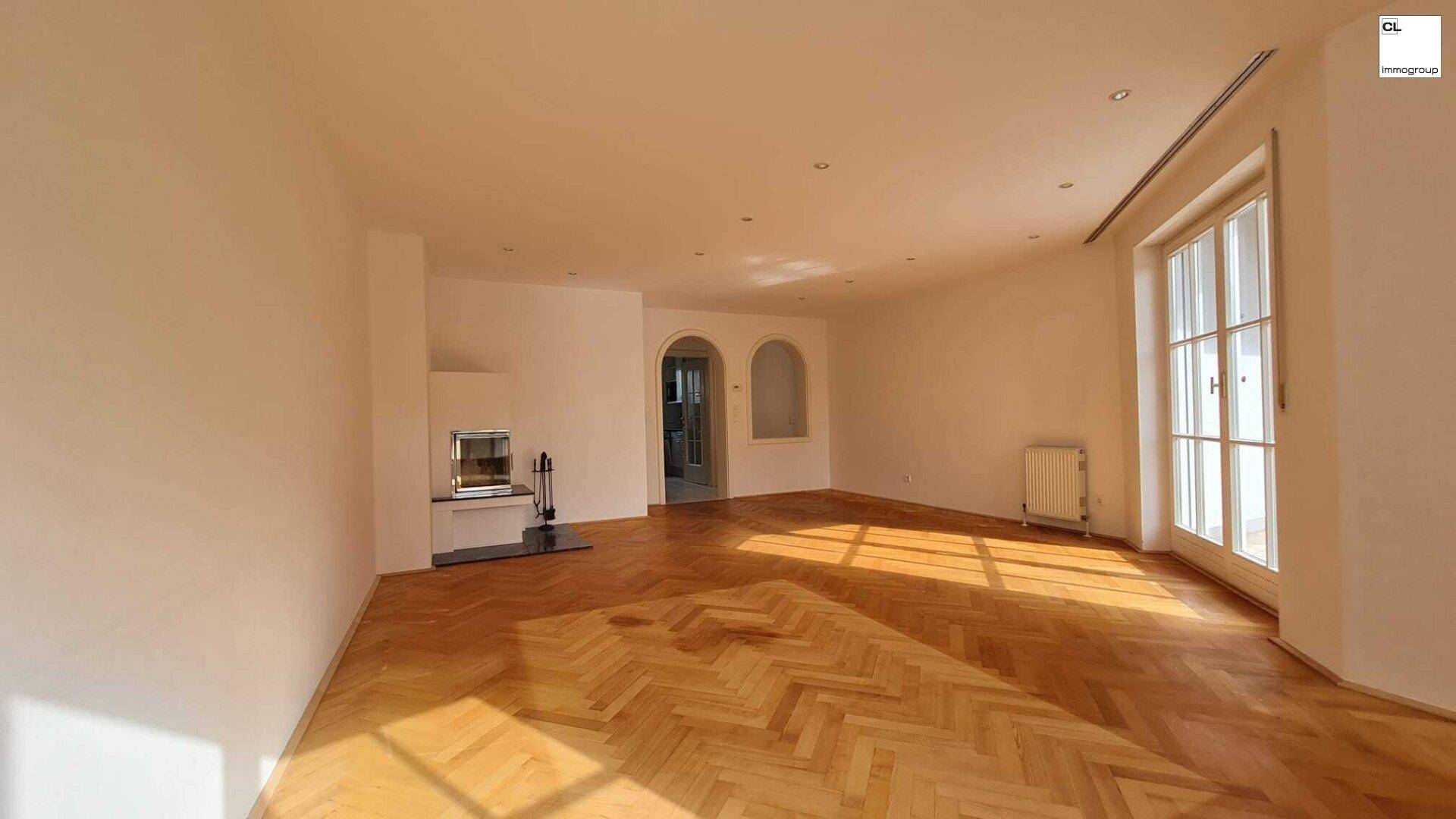Lichtdurchflutetes Wohnzimmer mit Kamin, Fischgrätparkett und großen Fenstern.