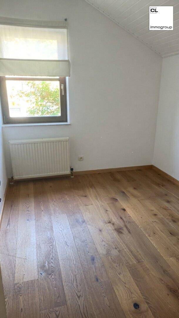 Gemütliches Zimmer mit Holzboden, Dachschräge und einem Fenster, das viel Licht hereinlässt.