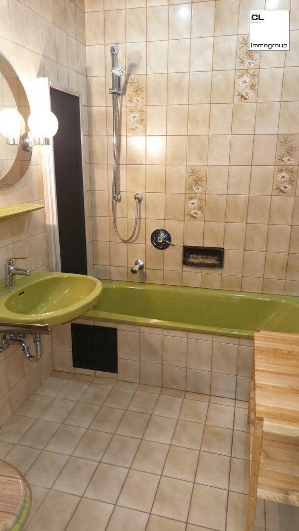 Badezimmer mit gelber Badewanne und Waschbecken, umgeben von beigen Fliesen und einer Duschvorrichtung.