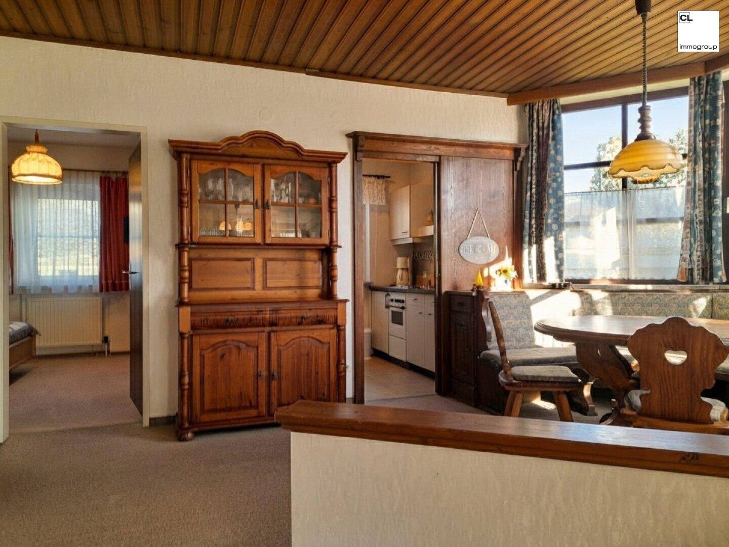Traditioneller Wohn- und Essbereich mit Holzdecke, Teppichboden und Blick in die angrenzende Küche.