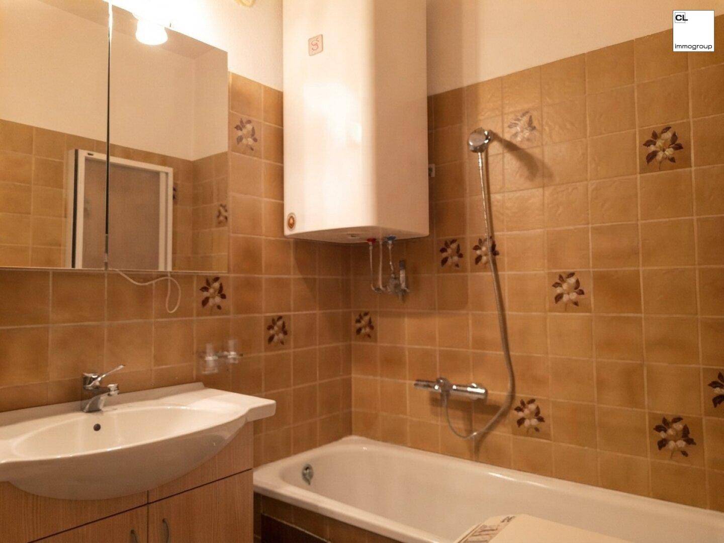 Gefliestes Badezimmer mit Badewanne, Waschbecken und Warmwasserboiler an der Wand.