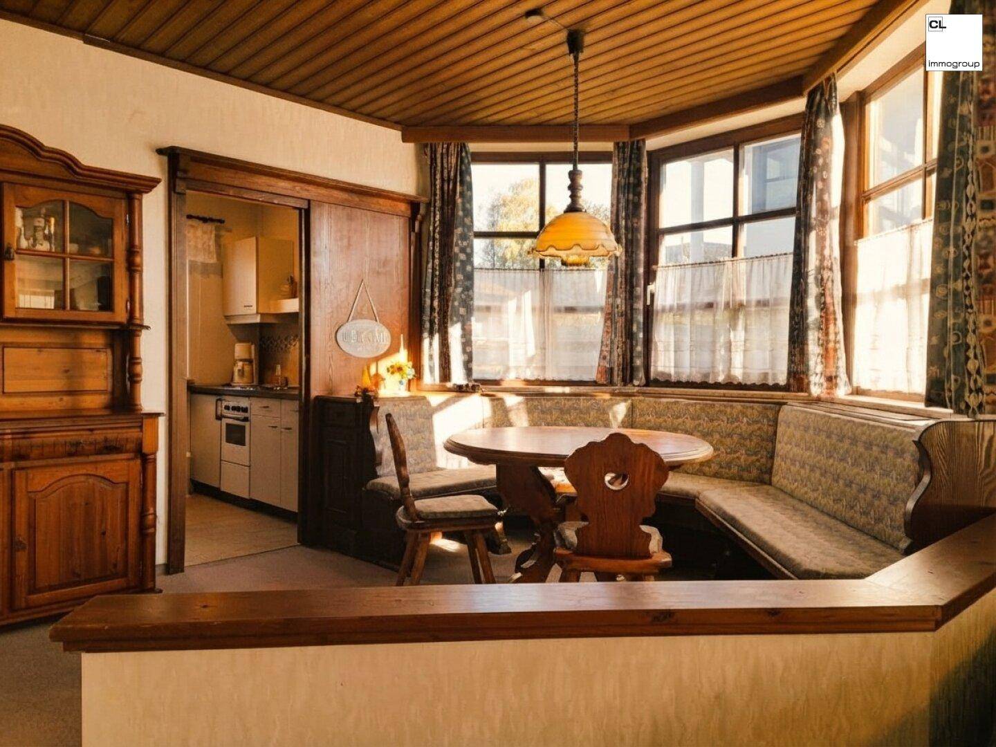 Traditioneller Wohn- und Essbereich mit Holzdecke, Teppichboden und Blick in die angrenzende Küche.