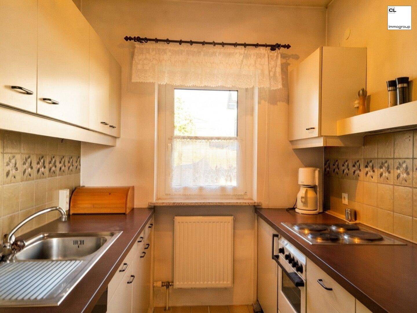 Funktionale Küche mit weißen Schränken, brauner Arbeitsplatte und einem Fenster.