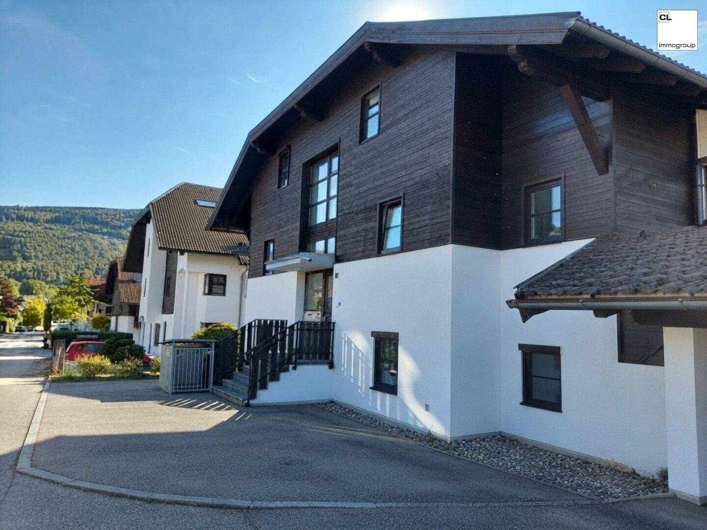 Modernes Gebäude mit dunkler Holzfassade und weißem Putz in sonniger Umgebung.