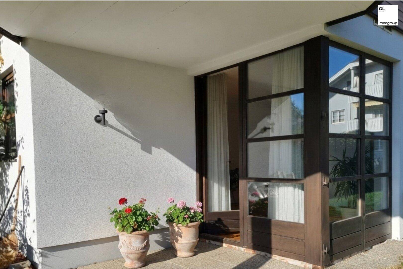 Überdachte Terrasse mit großen Fenstern und Topfpflanzen, die zum Entspannen einlädt.