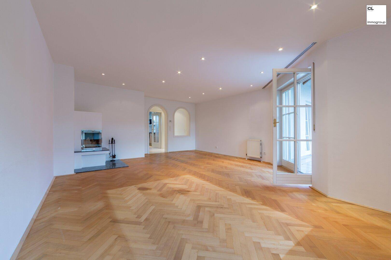 Geräumiges Wohnzimmer mit Fischgrätparkett, Kamin und Zugang zu einem Balkon.