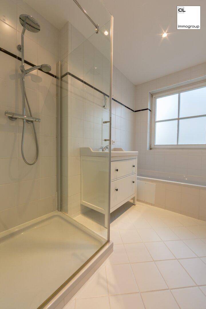 Helles Badezimmer mit Duschkabine, Badewanne und Fenster, ausgestattet mit weißen Fliesen.