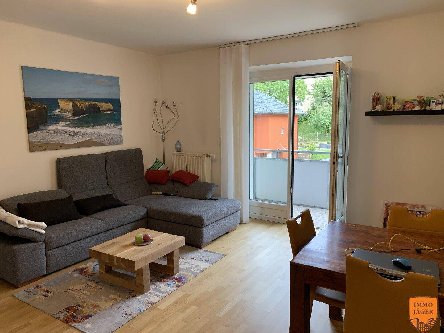 Gemütlicher Wohn-Essbereich mit Sofa, Holztisch und Zugang zu einem kleinen Balkon.