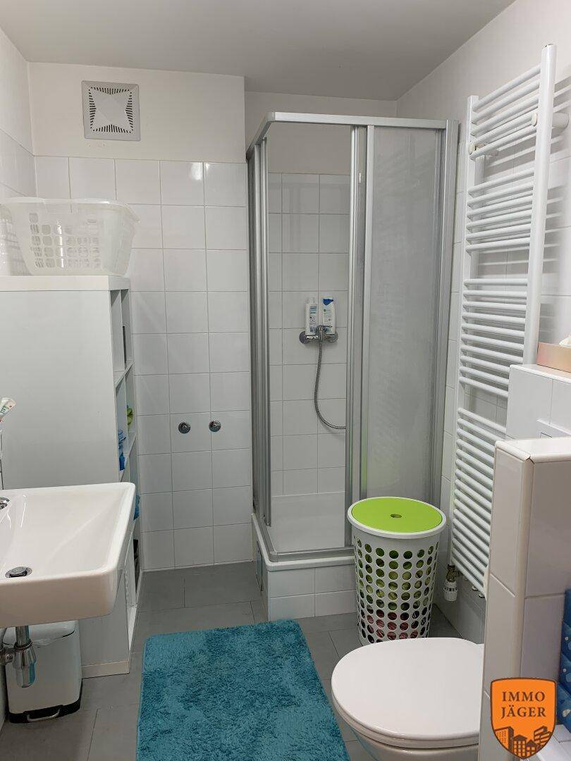 Helles Badezimmer mit Duschkabine, Waschbecken, WC und beheiztem Handtuchhalter.