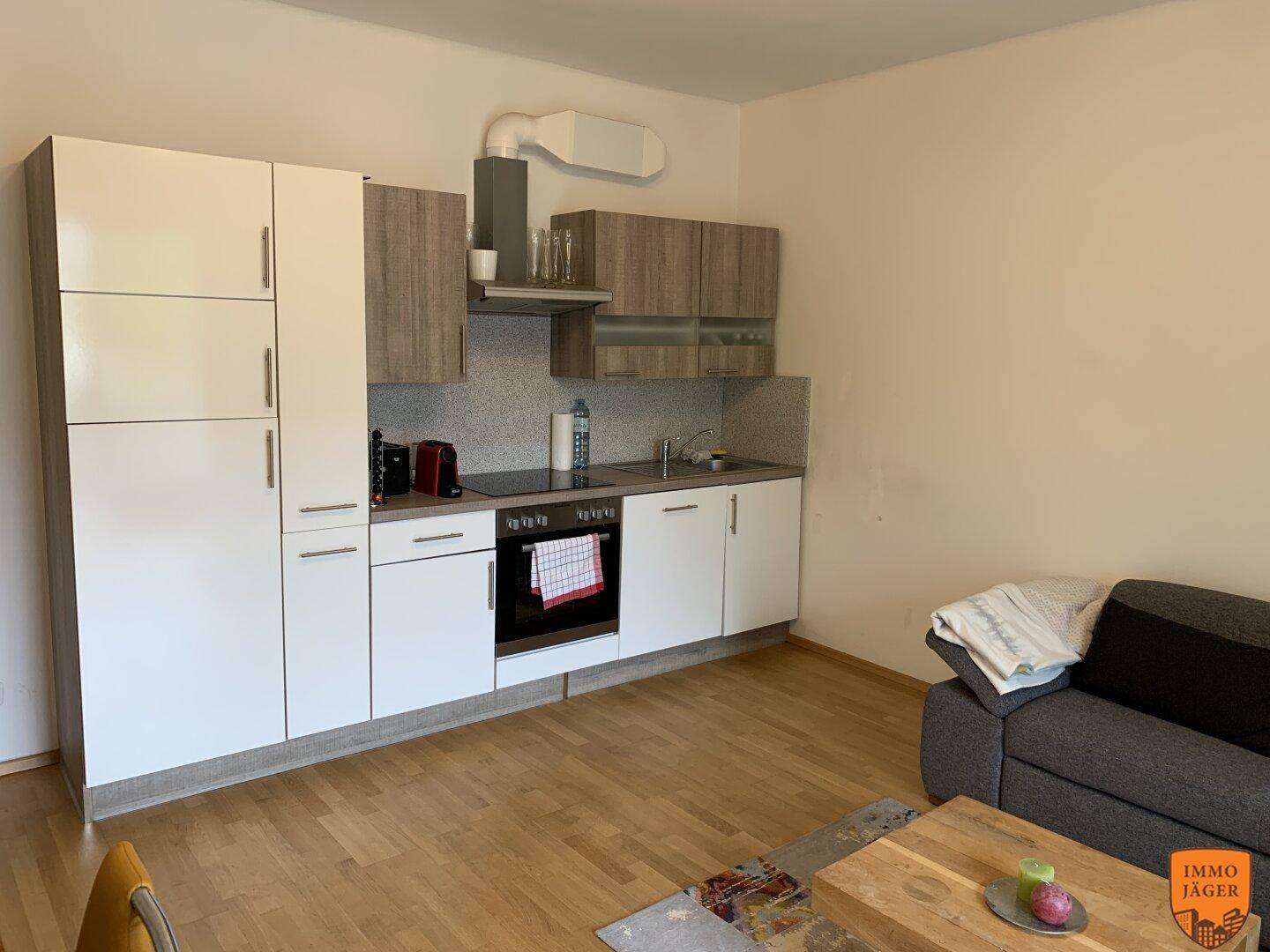 Kleine, moderne Küchenzeile mit weißen und holzfarbenen Schränken in einem offenen Wohnbereich.