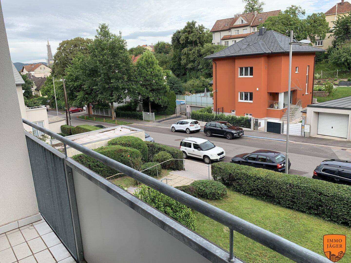 Balkon mit Blick auf die Straße, parkende Autos und eine Wohngegend mit Häusern.